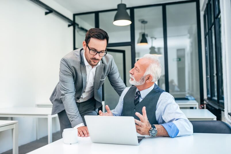 Junger Mann diskutiert mit Chef oder älterem Mitarbeiter in einem modernen Büro.